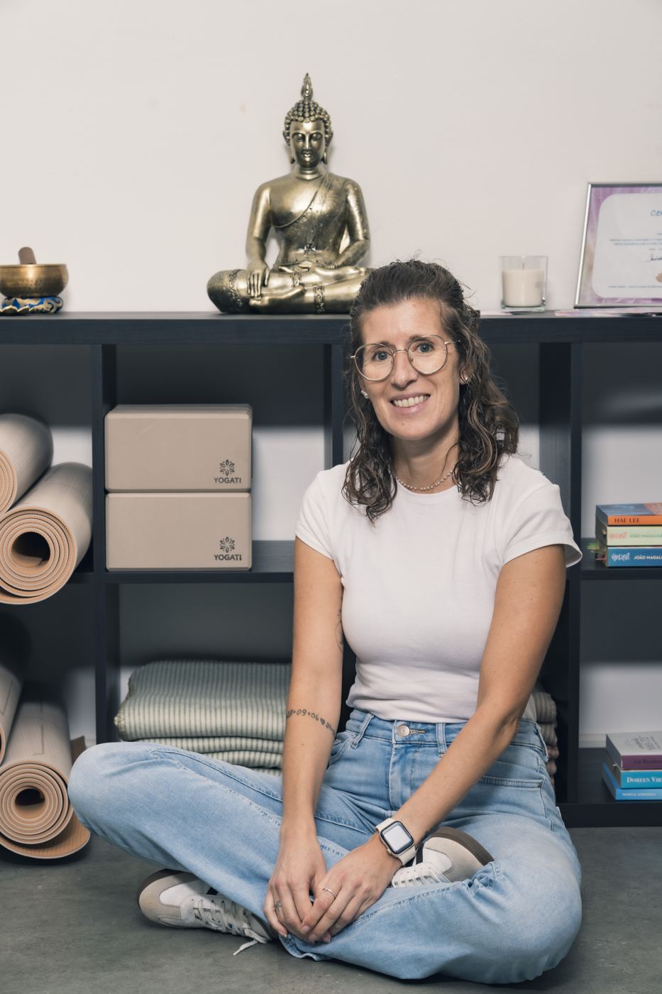 Sandra assise en tailleur devant les tapis et briques de yoga